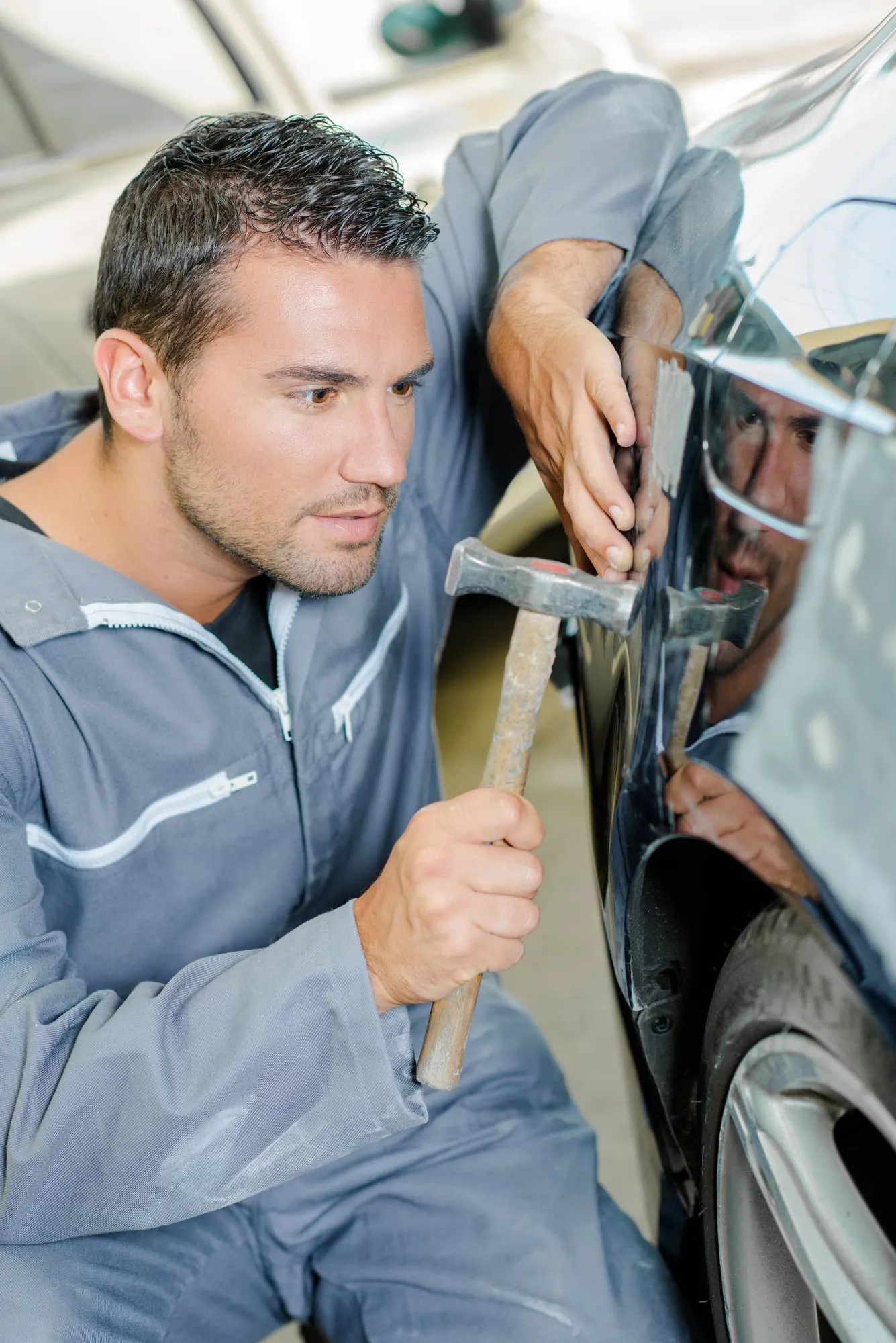 Panel beater repairing a dent in a car door